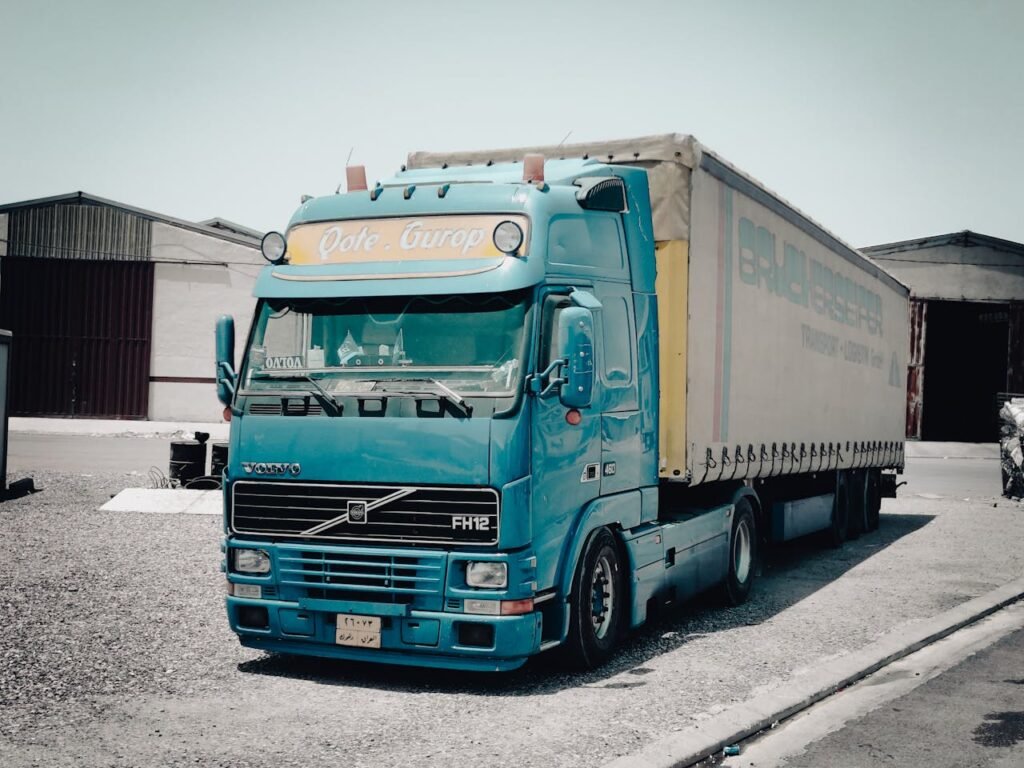 A blue Volvo truck parked outside a warehouse in an industrial area, daytime scene.
