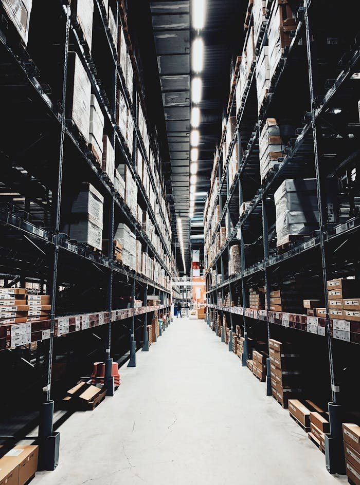 who-we-are A wide aisle in a large warehouse filled with stacked boxes on high shelves.